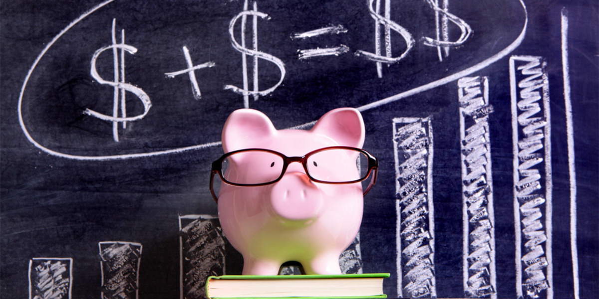 pink piggy bank sitting on top of a green book with dollar signs writing on a chalkboard